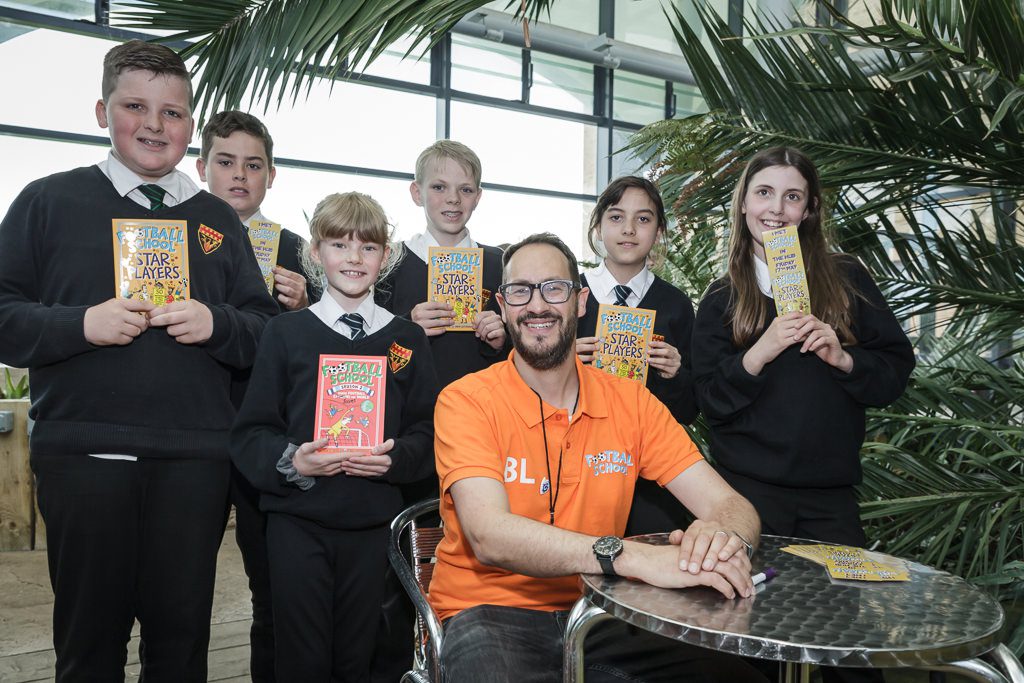 Group of student with the authors books with the author sitting at a table