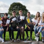 Students sitting on a bench looking happy with their exam results