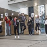 group of students jumping with 9 signs for their exam results