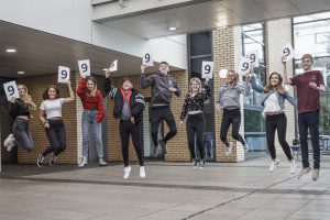 group of students jumping with 9 signs for their exam results