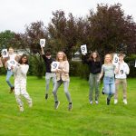 students jumping in the air holding 9 signs to celebrate their GCSE results